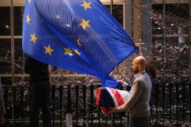 A man carrying a folded British flag next to two people removing a British flag from a flagpole.