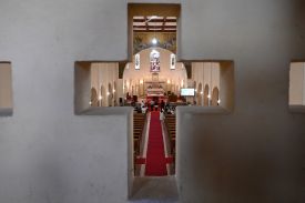 A cross-shaped opening shows nuns holding school lessons — a long red carpet extends forward into a church.