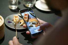 A camera on a smartphone shows a piece of chicken and waffle on a plate.