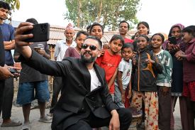Balendra Shah holds a phone to take a selfie with a group of children and supporters outdoors.