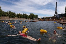 People float and swim in a river, with the Eiffel Tower in the background.