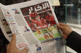 Two hands hold up a newspaper in Arabic. The lead photo shows the Moroccan soccer team on the pitch.
