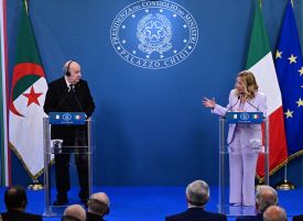 Tebboune (left) and Miloni look at each other as they both stand at podiums before their respective flags.