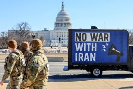 Three U.S. National Guard troops walk in front of a blue billboard truck that displays the message "No War With Iran" as it sits in front of the U.S. Capitol building.