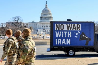 Three U.S. National Guard troops walk in front of a blue billboard truck that displays the message "No War With Iran" as it sits in front of the U.S. Capitol building.