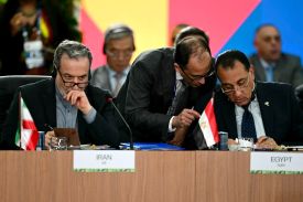 Iranian Foreign Minister Abbas Araghchi and Egyptian Prime Minister Mostafa Madbouly attend the BRICS summit. They are seated behind placards listing their countries and small national flags.