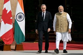 Carney and Modi walk side-by-side near Indian and Canadian flags. Both men smile slightly.