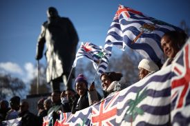 People stand in a line holding up Chagossian flags.