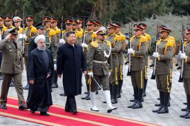 Rouhani and Xi stride down a red carpet side by side, while an honor guard in formal military uniforms stands at attention with rifles on the other side.
