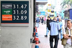 Pedestrians walk past a display with the prices in Hong Kong dollars at a gas station in Hong Kong.