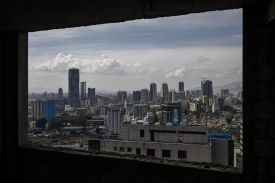 A skyline is shown from a window. There are skyscrapers, and it's a somewhat cloudy day.