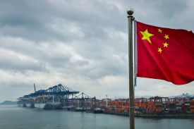 A Chinese flag is seen in the foreground with container ships, cranes, and shipping containers in Shenzhen, China, on April 12, 2025.