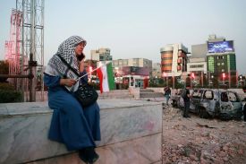 An Iranian woman sits close to a destroyed vehicle as she watches and listens to a traditional band as it performs to show solidarity with the Iranian people at Hafteh-tir Square, in Tehran on June 23, 2025.
