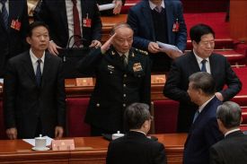Central Military Commission Vice Chairman Zhang Shengmin raises his right hand in a salute to Chinese President Xi Jinping, who is walking a level lower in a red-carpeted auditorium.
