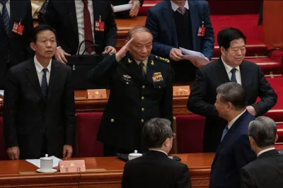 Central Military Commission Vice Chairman Zhang Shengmin raises his right hand in a salute to Chinese President Xi Jinping, who is walking a level lower in a red-carpeted auditorium.