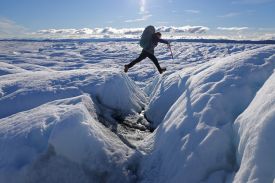 A woman wearing a large backpack crosses a rift in an ice sheet.