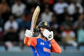 Abhishek Sharma, a player for India's national cricket team, is dressed in official sport attire while holding a bat.