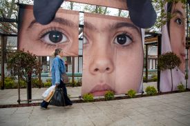 A woman passes an art installation featuring portraits of some of the school girls killed in an apparent U.S. strike in February, in Tehran.