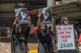 Two protesters hold up portraits of Khamenei's face, while a third holds a sign that reads: "WE STAND WITH THE PEOPLE OF IRAN."