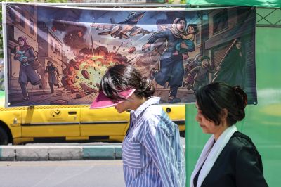 Women in Tehran are seen walking on the street past a banner that depicts U.S. and Israeli strikes on Iran.