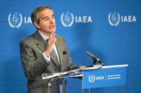 Rafael Grossi, the director-general of the International Atomic Energy Agency, stands in from of a podium with a microphone. He is speaking to journalists (not seen in frame). His right hand gestures as he talks.