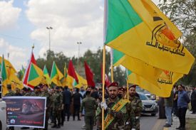 Waving yellow and green flags and wearing uniforms, Members of Iraqi pro-Iran paramilitary group Kataeb Hezbollah gather in a mourning procession.