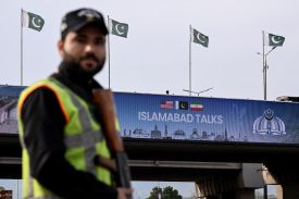 A police man in a hi-vis vest stands in front of a sign advertising peace talks in Islamabad.