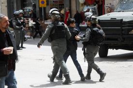 Two soldiers in uniform flank a young man as they walk down the street.