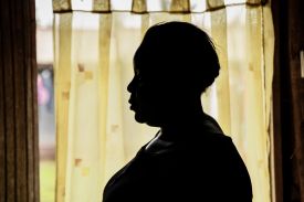 The silhouette of a woman in front of a yellow curtain.