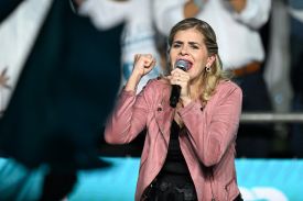 Costa Rican presidential candidate Laura Fernandez gestures as she speaks into a microphone. She is wearing a pink jacket.