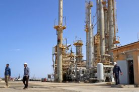 A handful of workers in hardhats are shown at an oil field in daylight.