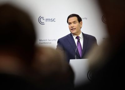 Rubio is shown speaking at a podium ahead of a white background.