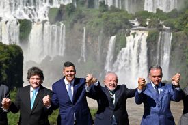 The president of Argentina, Paraguay, Brazil, and Uruguay stand holding hands in front of a waterfall.