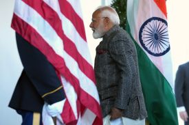 Modi is seen in profile as he walks between an American and Indian flag while heading into the White House. A U.S. service member in dress uniform stands in the doorway, partly obscured by the U.S. flag.