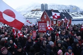 A large crowd of people dressed in thick winter coats, with some waving Greenlandic flags and others holding placards that read, "Greenland is not for sale!" stands outside the U.S. consulate in Nuuk, Greenland.