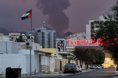 An Emirati flag flies next to a plume of smoke and next to a red neon sign that reads "Century Mall."