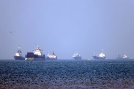 Six larger vessels are anchored in the Strait of Hormuz. A small speedboat drives past them.