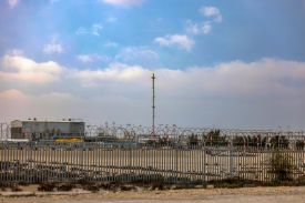 A tower topped with a flame behind rows of fences.
