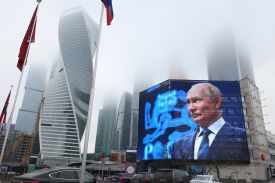 A building has a large screen with an image of Vladimir Putin against a backdrop of skyscrapers on a gloomy day.