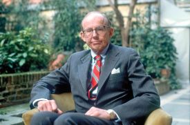 A seated man wearing glasses and a suit.