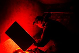 A soldier is seen at night in dark room illuminated by red light as he uses a Starlink device.
