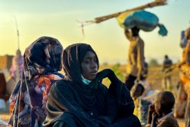 A woman looks into the distance. She's sitting in a group of other people.