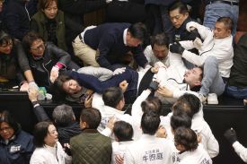 About a dozen lawmakers and aides are seen from overhead as they brawl on the floor of a legislative chamber, throwing arms, pulling on shirts, and shouting. One man is nearly horizontal as he's hauled over a low wall.