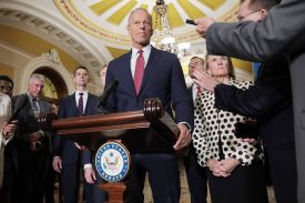 U.S. Republican Senate Majority Leader John Thune speaks at a podium inside the U.S. Capitol while surrounded by reporters and other Republican senators in his leadership team.