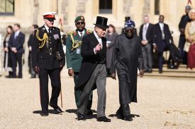 King Charles III and Bola Tinubu walk side by side; a small crowd of people stands behind them.
