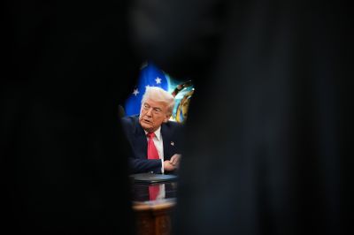 Donald Trump is sett through an opening as he sits at a desk.
