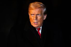 Trump is seen from the chest up against a dark nighttime background, which makes it appear that his head is floating against a background of deep black. He wears a dark suit, red tie, and a serious expression.