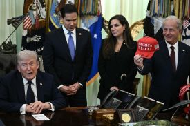 Rubio, Hamadeh, and Issa stand behind Trump's desk in the Oval Office while Trump speaks with his hands clasped on the desk's surface. All three of the standing officials wear smiles of various sizes, and Issa brandishes a hat toward Trump.
