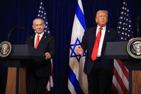 Trump holds stands near a lectern next to Netanyahu, who has his hand on his podium. Both men are wearing business suits and red ties. The lecterns show the U.S. presidential seal, and behind them are U.S. and Israeli flags.