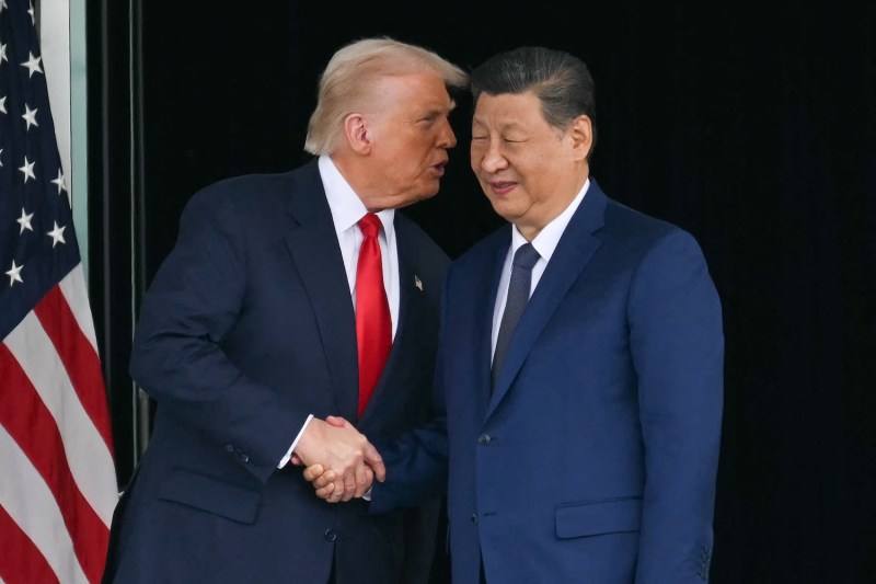 Trump (left) and Xi (right) shake hands, while Trump appears to be whispering something into Xi's ear.
